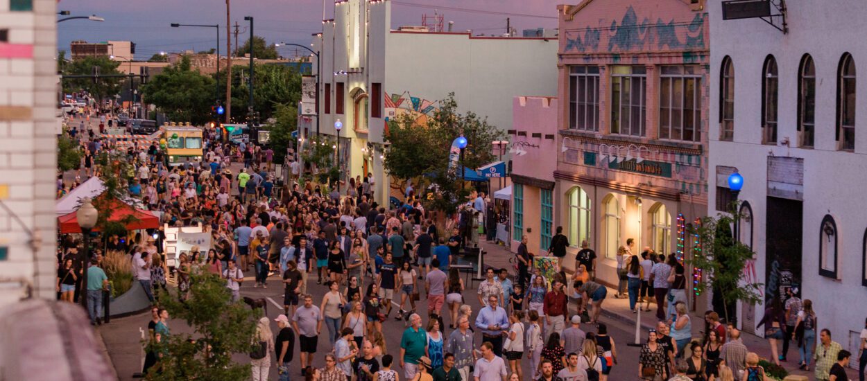 People fill the street at sunset and engage with arts and culture.