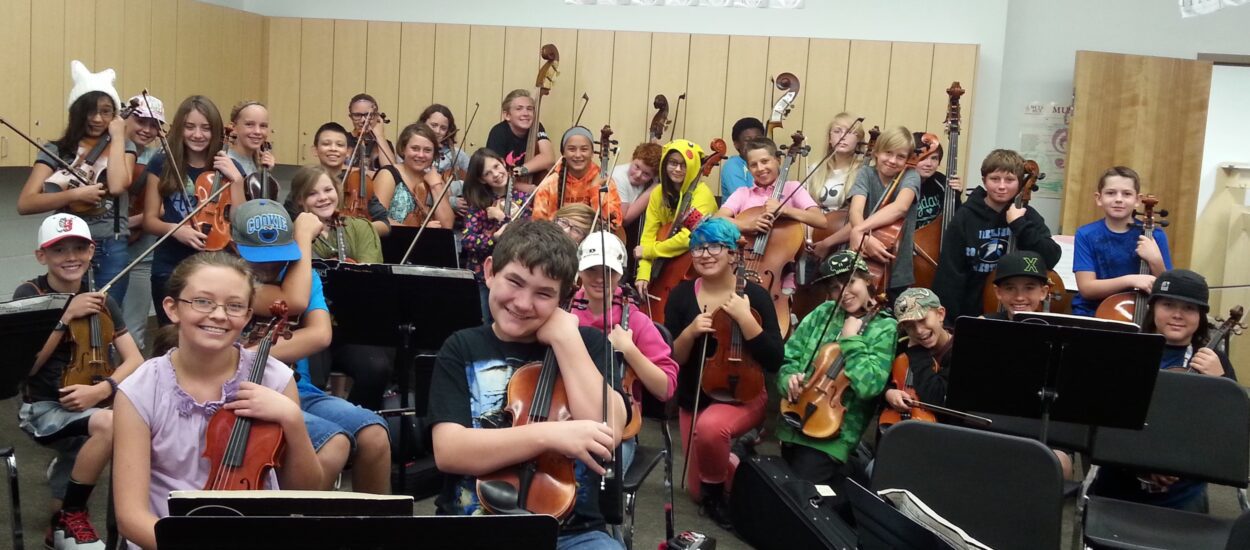 Students at East Middle School post with their musical instruments in a music classroom
